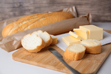 Tasty cut baguette with fresh butter on white table