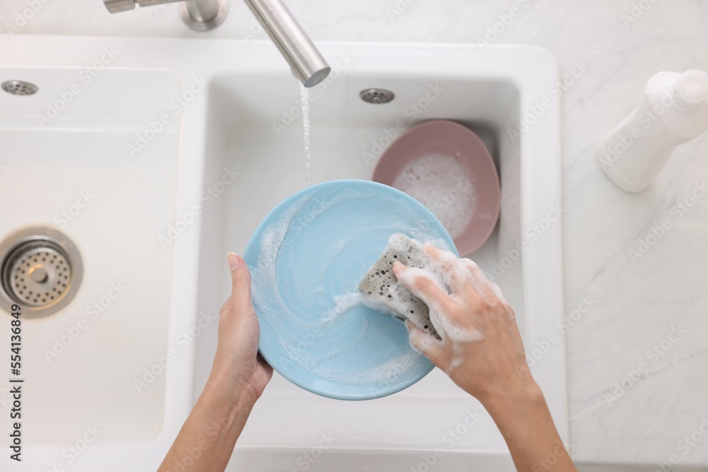 Sticker Woman washing plate above sink in modern kitchen, top view