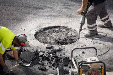 hydraulic hammer in the hands of an operator in uniform works the asphalt, partner collects rubble