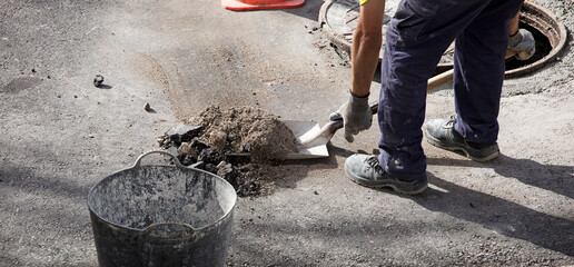 shovel with stone rubble in the hands of an operator in uniform cutting the asphalt ground, dust in...