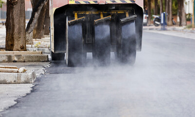 asphalt paving machines with big wheels, smoke vapor from freshly made hot concrete