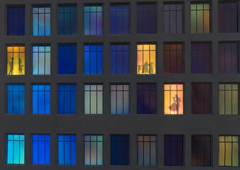 Fototapeta na wymiar the wall of a night house in the illuminated windows of which silhouettes of people are visible