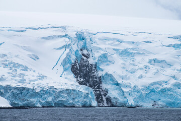 The jagged rock was exposed after calving an iceberg.  The dark rock contracts to the glacier blue and white snow in Antarctica. 