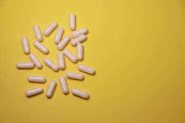 close up of white pills capsules on yellow background