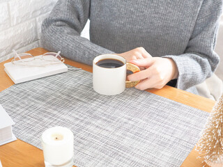 くつろぎながらコーヒーを飲むニットの女性