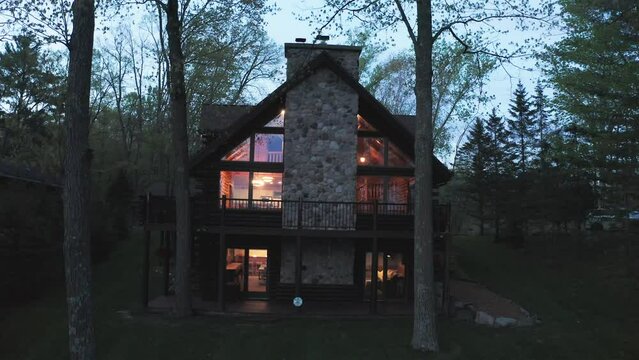 Aerial, exterior of wealthy expensive wooden cabin in the forest in the evening, lights on