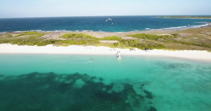 Aerial shot rider ready to kiteboard on turquoise caribbean sea near motorboat and white sand beach, LOS ROQUES