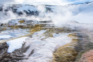 Mammoth Hot Springs Terraces with great detail of  travertine and thermal steam in yellow and white, covered by snow with sky and cloud as background
