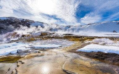 Mammoth Hot Springs Terraces with thermal pond and limestone cascade in yellow and white, covered by snow with sky and cloud as background