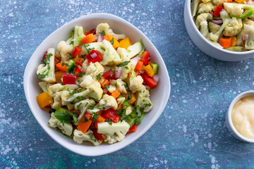 Healthy cauliflower salad in white bowl on blue wood background.
