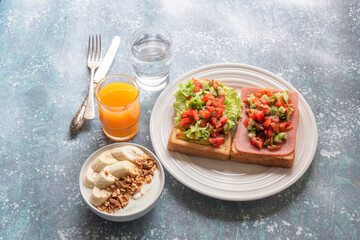 Sandwich breakfast has ham cheese and tomato cucumber and yoghurt on blue wood table.
