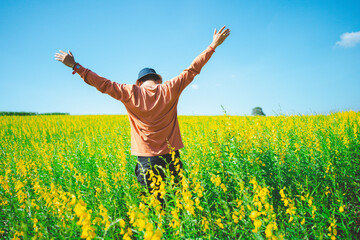 Rear view of a happy freedom man raising his hands up in nature yellow flower field.