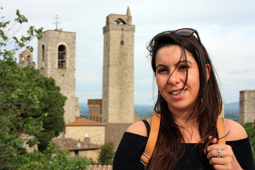 young brunette caucasian woman in front of the panorama of san gimignano, romantic medieval tuscan city in stone and red bricks