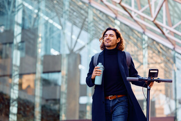 Young Hispanic businessman pushing electric scooter while walking through city.