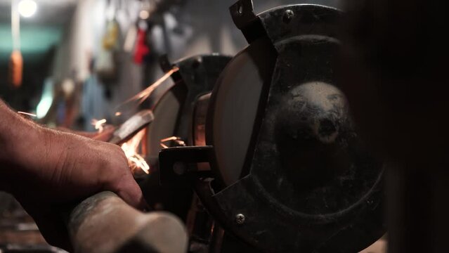 Sharpening an ax on an electric grinding wheel, Machine sharpening an ax on an electric grinder, hand sharpening on a rotating grinding stone, close-up.