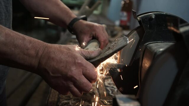 Sharpening an ax on an electric grinding wheel, Machine sharpening an ax on an electric grinder, hand sharpening on a rotating grinding stone, close-up.