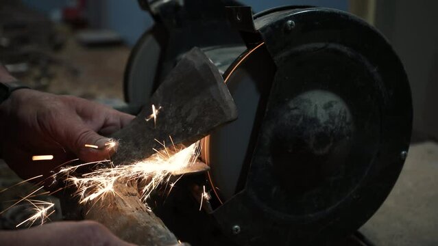 Sharpening an ax on an electric grinding wheel, Machine sharpening an ax on an electric grinder, hand sharpening on a rotating grinding stone, close-up.