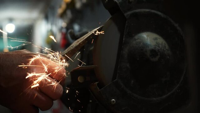 Sharpening an ax on an electric grinding wheel, Machine sharpening an ax on an electric grinder, hand sharpening on a rotating grinding stone, close-up.