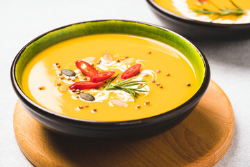 Spicy pumpkin cream soup garnished with seasoning and red chili pepper. Thick butternut squash bisque in green bowl over concrete table. Minimal style. Selective focus