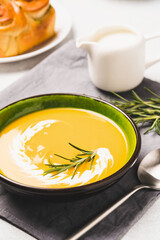 Bowl of pumpkin cream soup with garlic buns and heavy cream. Thick butternut squash bisque in green bowl garnished with heavy cream and rosemary.  Vertical image, selective focus