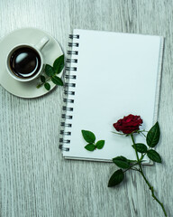 An open notebook with white sheets. An office desk with a notepad, a red rose and a cup of coffee. Flat layout, top view, place to copy. Space for text. Selective focus.