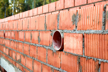 Works on the laying of ceramic bricks. Red brick wall with ventilation hole. Embedded detail in the wall. Progressive construction of walls and partitions.