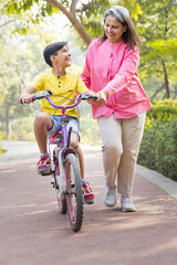 Fototapeta premium Grandmother trying to teach grandson to ride a cycle at park.