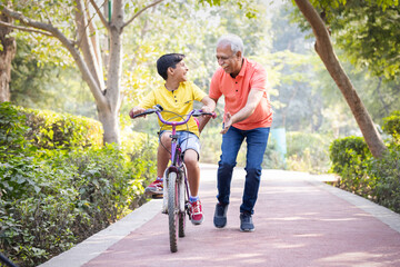 Grandfather trying to teach grandson to ride a cycle at park.