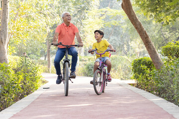 Happy grandfather and grandson riding bicycle at park.