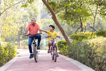 Happy grandfather and grandson riding bicycle at park.