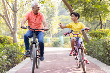 Happy grandfather and grandson riding bicycle at park.