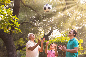 Three generation family having fun while playing with ball at park.