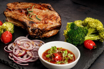 Close-up BBQ pork loin with spicy sauce and vegetables on a black stone board. Selective focus. Old rustic wooden background