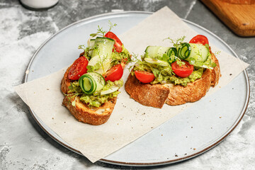 Appetizing sandwiches with avocado, cucumber, cherry tomatoes and herbs. Toast with guacamole sauce and fresh vegetables. Vegetarian breakfast or snack. Delicious and healthy food.