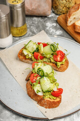 Appetizing sandwiches with guacamole sauce and fresh vegetables. Toast with avocado, cucumber, cherry tomatoes and herbs. Vegetarian breakfast or snack. Delicious and healthy food. Vertical shot