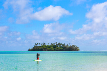 Man paddleboarding towards a tiny tropical island in the middle of a big lagoon. Photographed at Muri, Rarotonga, Cook Islands
