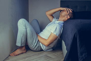 Depressed man sitting on the floor with his head down and leaning against the wall. In frustrated feelings. The concept of mental disorders. Schizophrenia, psychosis, fear.