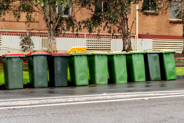 Fototapeta na wymiar Australian garbage wheelie bins with yellow and red lids for recycling and household waste lined up on the street near residential building for council rubbish collection.