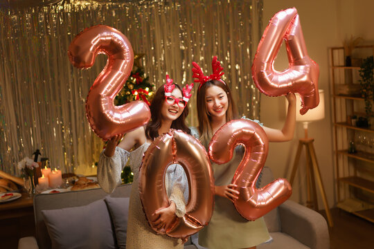New Year celebration concept, Two beautiful women holding balloon pink gold number 2024 in party