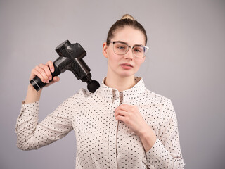 A caucasian woman uses a massager gun for pain in the muscles of her back and shoulders.