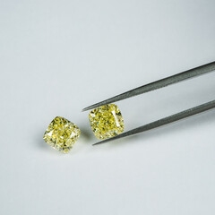 Cushion fancy yellow diamonds compare with tweezers on white surface