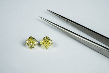 Cushion fancy yellow diamonds compare with tweezers on white surface