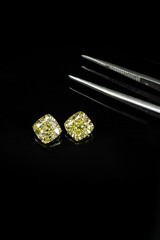 Cushion fancy yellow diamonds compare with tweezers on black reflection surface