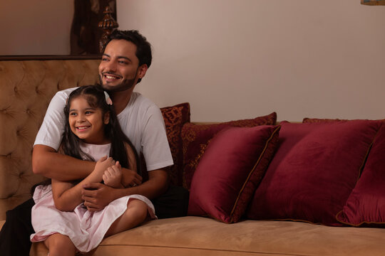 Father and daughter sitting on deewan and looking elsewhere