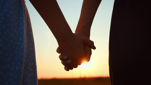 Close-up romantic view of couple holding hands against blurred sky and sunset. Relationships, support and love. Overcoming difficulties. Happy family travel. Date on outdoors nature landscape.