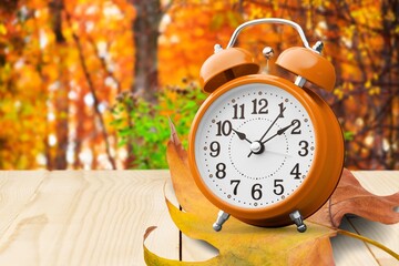 Alarm retro clock with autumn dry leaf on desk