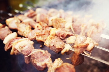 Selective focus. Cooking barbecue on the mangal in nature. Grilled tasty meet cooking on the party. Traditional Russian shashlik on a barbecue skewer on sunny forest.