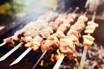 Selective focus. Cooking barbecue on the mangal in nature. Grilled tasty meet cooking on the party. Traditional Russian shashlik on a barbecue skewer on sunny forest.