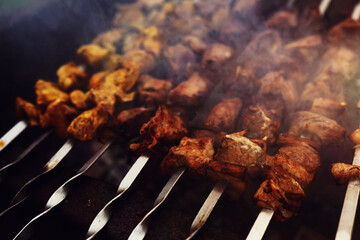 Selective focus. Cooking barbecue on the mangal in nature. Grilled tasty meet cooking on the party. Traditional Russian shashlik on a barbecue skewer on sunny forest.