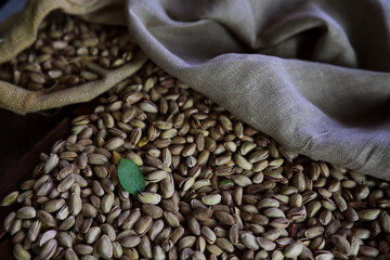 Pistachio nut in sack bag with mint green leaf on wooden table background.